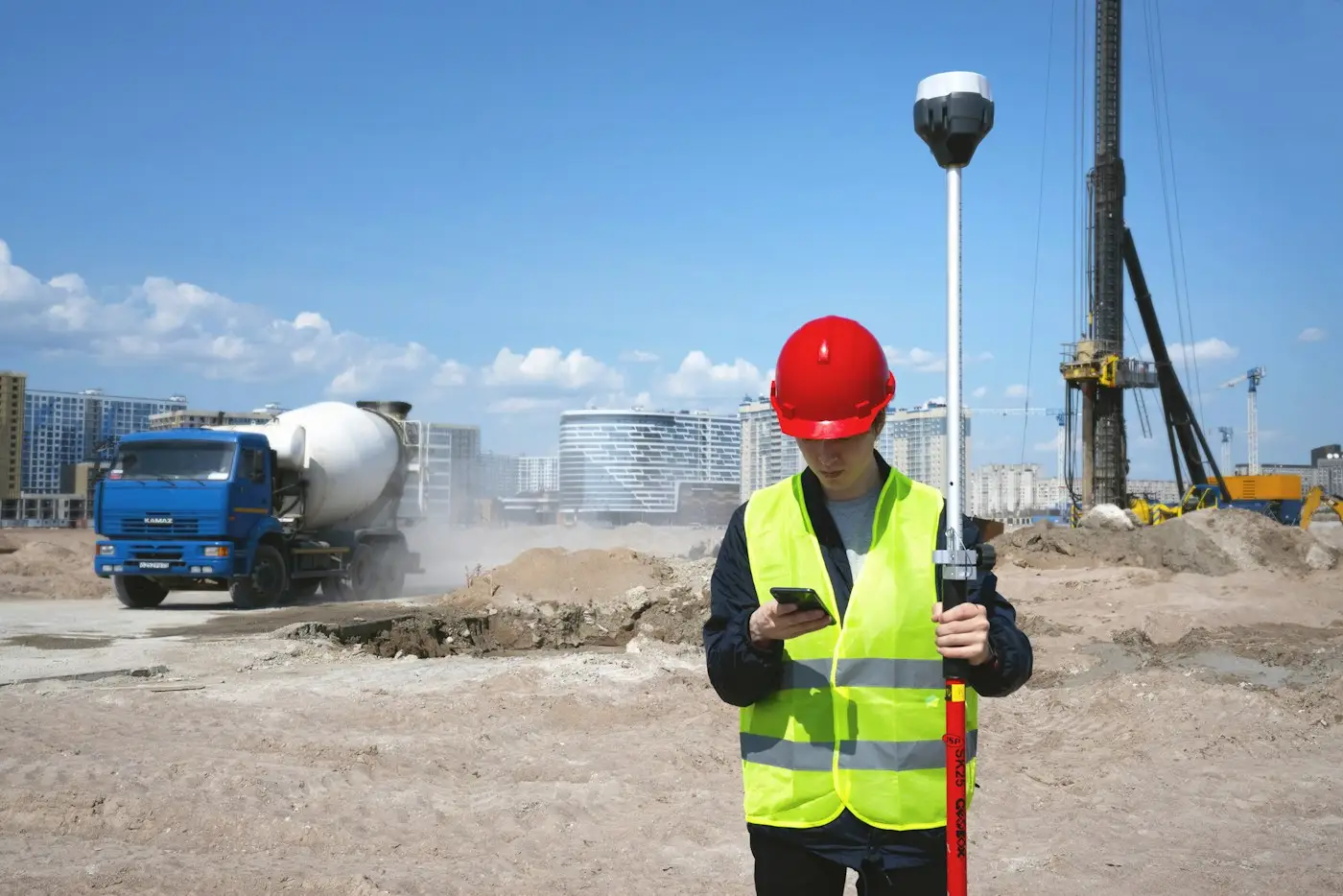 A site engineer in a hard hat with a GPS rover on a busy site