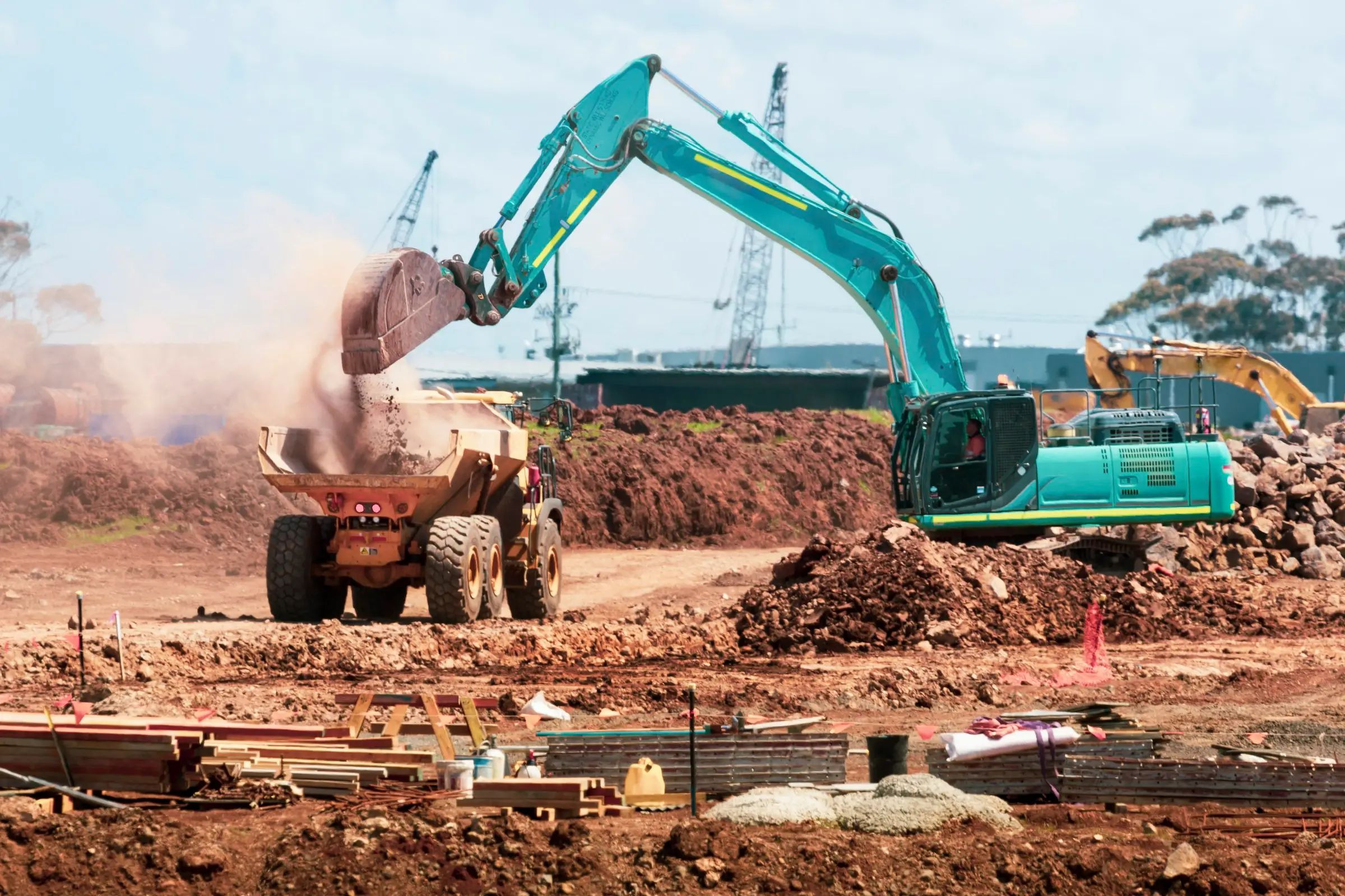 An excavator tipping soil into a dumper on a site being cleared for building