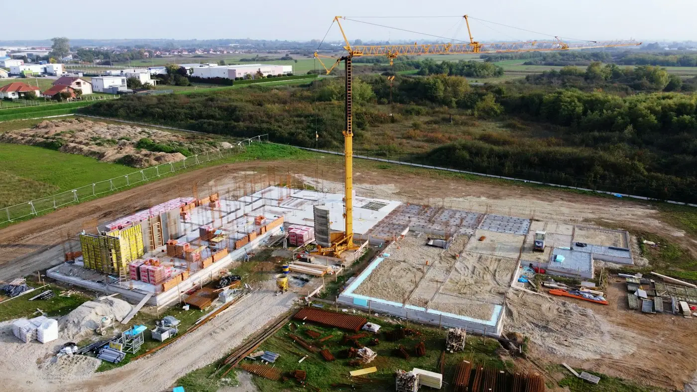An aerial view of a large building site, with a tower crane and the first walls going up