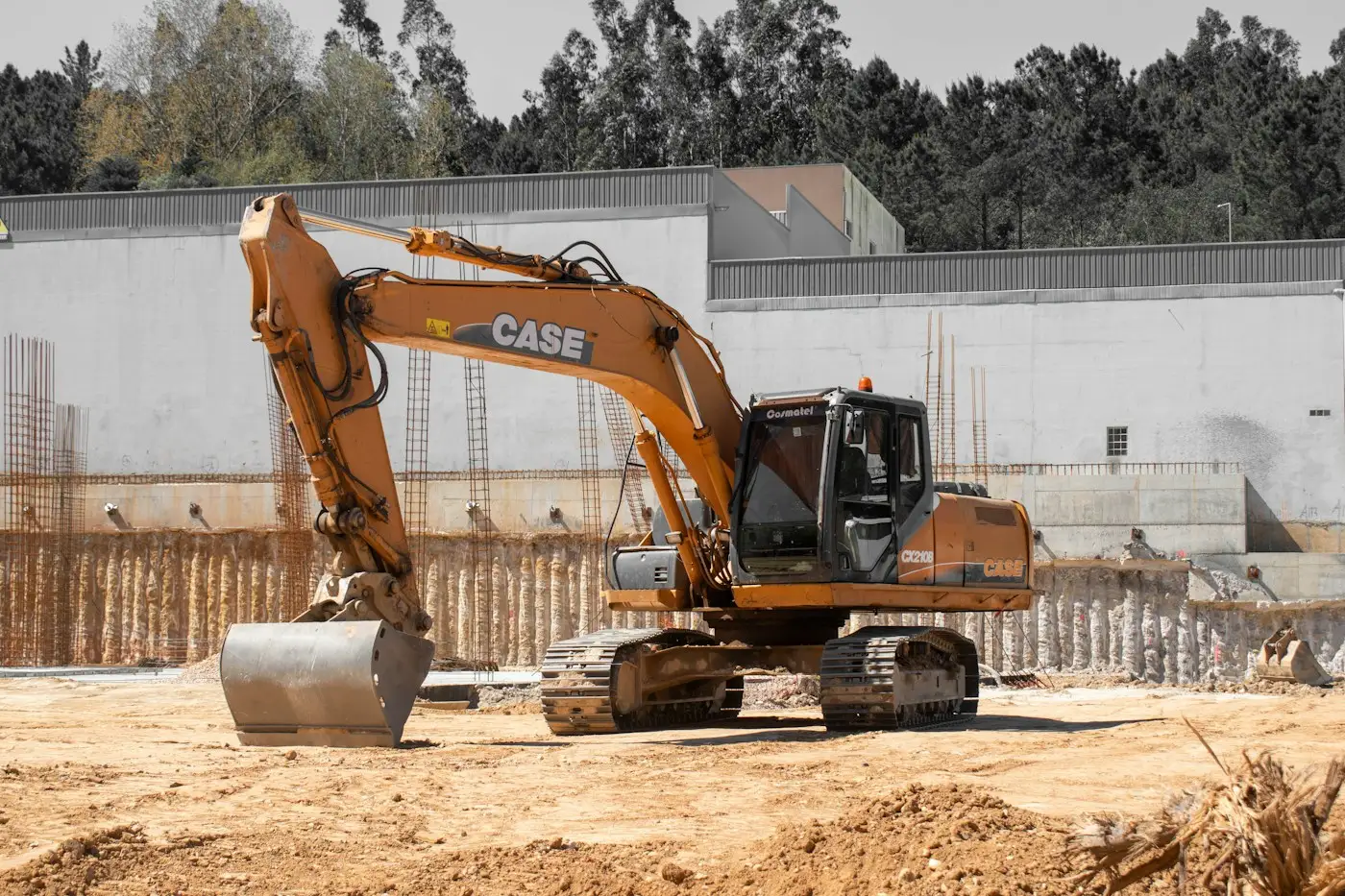A tracked excavator on a site, with a retaining wall behind