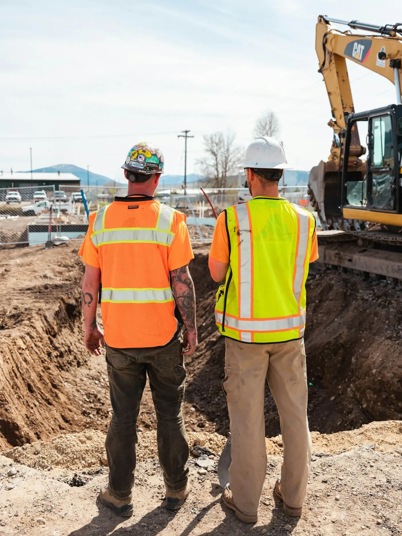 Two groundworkers in hi-vis checking a trench beside an excavator